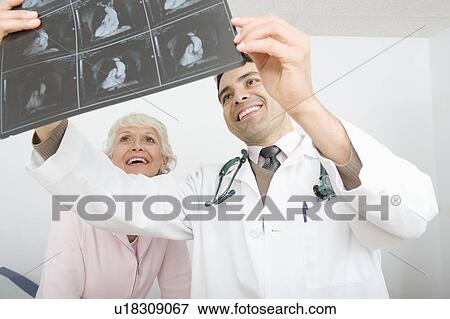 Mid adult doctor examines x-ray for senior patient View Large Photo Image Stock Photo - Mid adult doctor examines x-ray for senior patient. Fotosearch