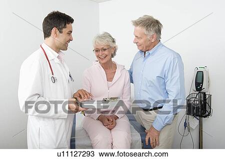 Stock Image - Mid adult doctor explains test results to senior couple. Fotosearch