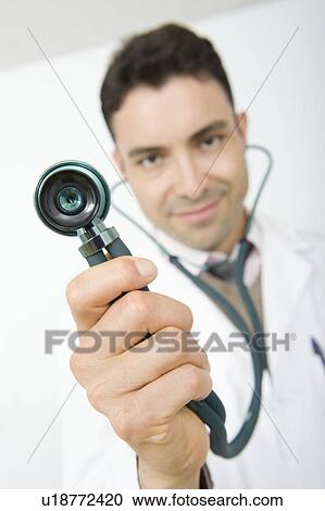 Stock Image - Mid adult doctor smiling and holding stethoscope. Fotosearch
