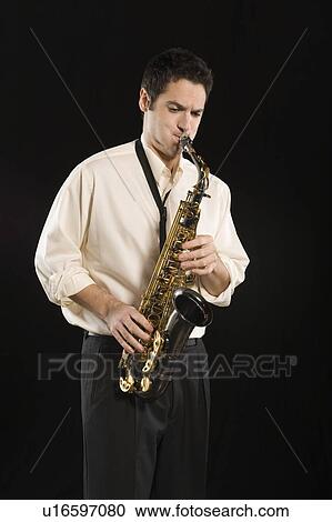 Stock Image - Mid adult man stands in shirt playing the saxophone. Fotosearch