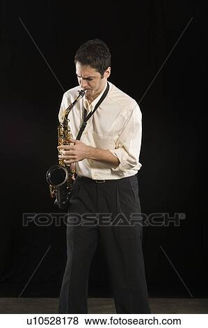 Stock Photo - Mid adult man stands in shirt playing the saxophone. Fotosearch