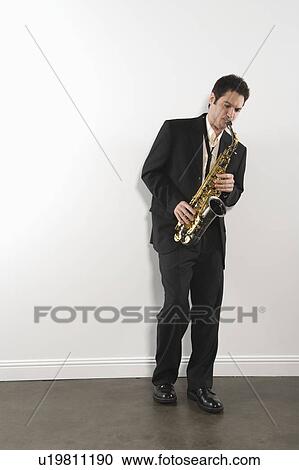 Mid adult man stands in suit playing the saxophone View Large Photo Image Stock Image - Mid adult man stands in suit playing the saxophone. Fotosearch