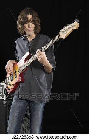 Stock Photo - Mid adult man stands playing an electric guitar. Fotosearch