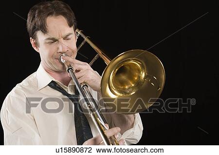 Stock Image - Mid-adult man with open-collar shirt plays the trombone. Fotosearch