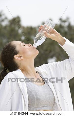 Mid adult woman drinking mineral water View Large Photo Image Picture - Mid adult woman drinking mineral water. Fotosearch