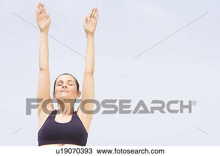 Stock Image - Mid adult woman stretches arm up with eyes closed. Fotosearch