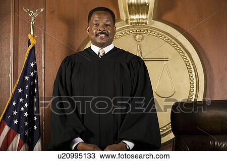 Stock Image - Middle-aged judge standing in a courtroom. Fotosearch