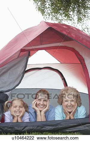 Stock Image - Mother, daughter and grand-daughter lean on elbows, smiling from tent. Fotosearch