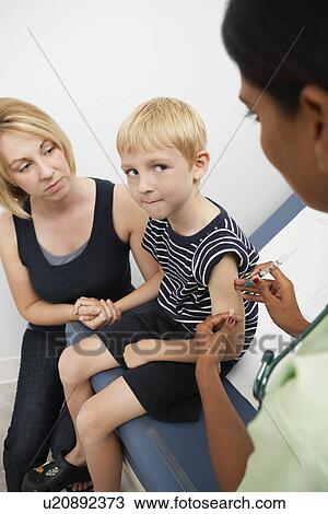 Stock Image - Mother supporting son receiving injection, elevated view. Fotosearch