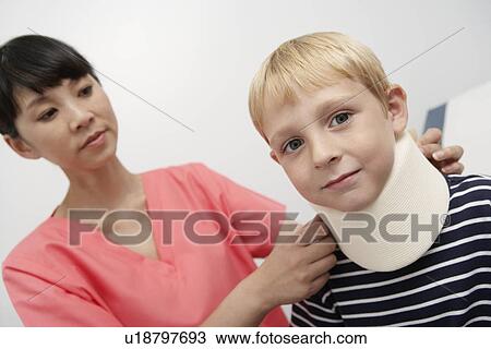 Stock Image - Nurse assisting boy wearing neck brace in hospital. Fotosearch
