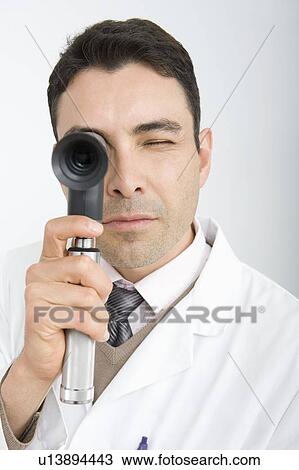 Stock Image - Optician looks through sight testing equipment. Fotosearch