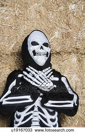 Stock Image - Portrait of child (7-9) wearing skeleton costume by hay. Fotosearch