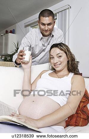 Stock Photo - Portrait of expectant couple, man serving glass of milk to woman. Fotosearch