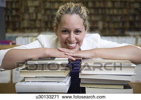 Stock Image - Portrait of female librarian with stacked books. Fotosearch