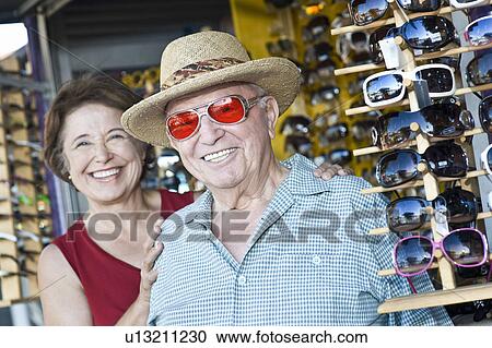 Stock Image - Portrait of senior couple trying on sunglasses, smiling. Fotosearch