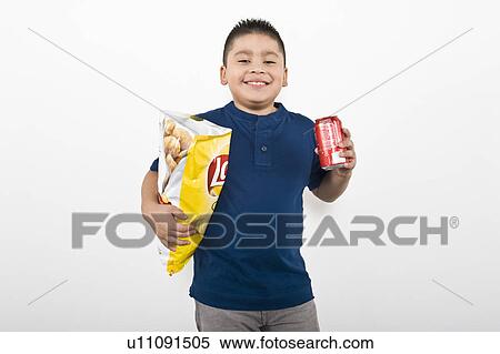 Stock Photography - Pre-teen (10-12) boy holding bag of potato chips and drink can. Fotosearch