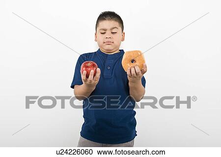 Stock Image - Pre-teen (10-12) boy holding doughnut and apple. Fotosearch
