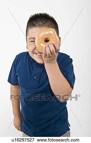 Stock Photo - Pre-teen (10-12) boy holding doughnut over eye. Fotosearch