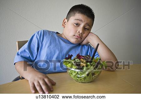 Stock Image - Pre-teen (10-12) boy sitting at desk with salad. Fotosearch