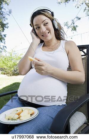 Pregnant woman listening to music and eating apple outdoors View Large Photo Image Stock Photo - Pregnant woman listening to music and eating apple outdoors. Fotosearch