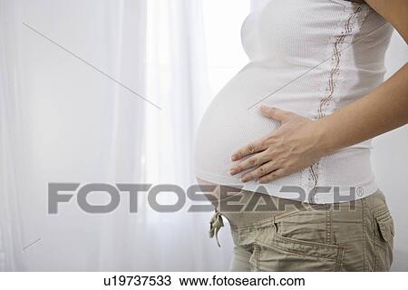 Pregnant woman standing by window, mid section View Large Photo Image Stock Image - Pregnant woman standing by window, mid section. Fotosearch
