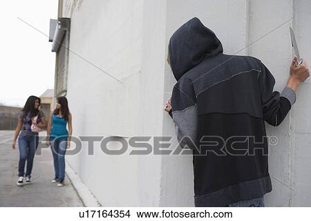 Picture - Robber with knife hiding behind corner and waiting for two girls. Fotosearch