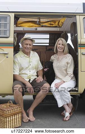 Picture - Senior couple sit in campervan with pet their dog. Fotosearch