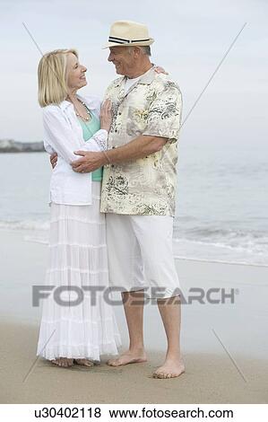 Stock Photo - Senior couple stand embracing on beach. Fotosearch