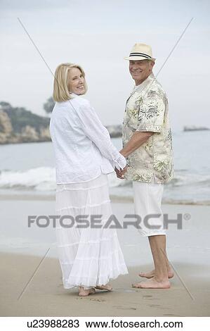 Senior couple stand holding hands on beach View Large Photo Image Stock Image - Senior couple stand holding hands on beach. Fotosearch