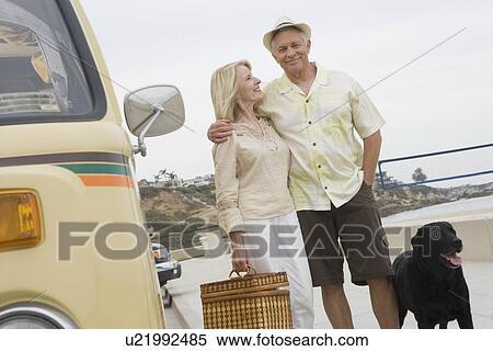 Stock Photography - Senior couple stand on beach promenade with campervan. Fotosearch