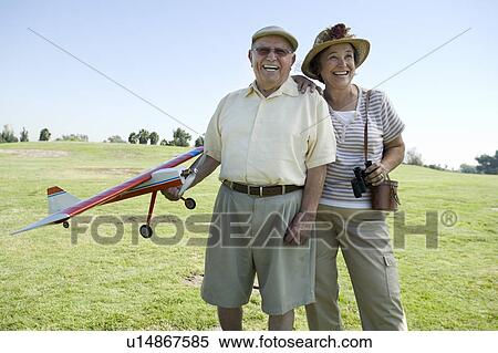 Stock Photography - Senior couple standing on field, man holding model plane. Fotosearch