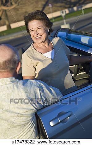 Stock Image - Senior couple standing outside convertible, elevated view. Fotosearch