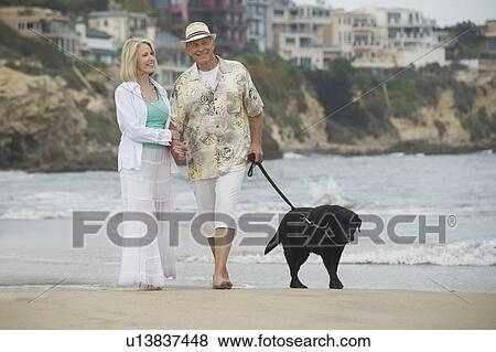 Stock Photo - Senior couple walk dog on beach. Fotosearch