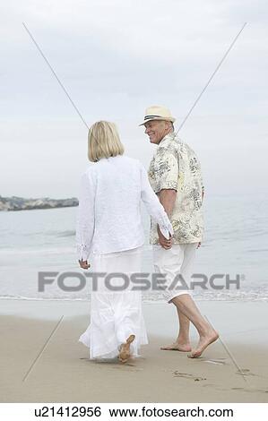 Senior couple walk holding hands on beach View Large Photo Image Stock Photograph - Senior couple walk holding hands on beach. Fotosearch