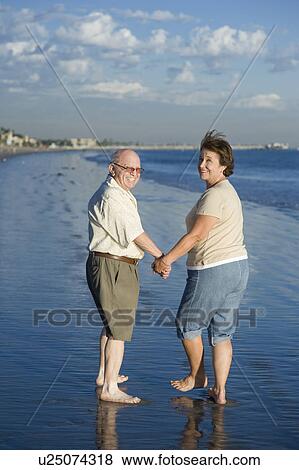 Stock Photo - Senior couple walking on beach, looking back. Fotosearch