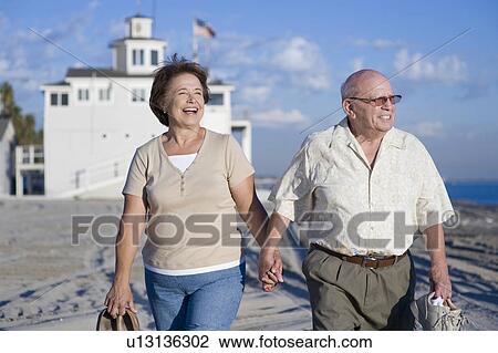 Stock Image - Senior couple walking on beach. Fotosearch