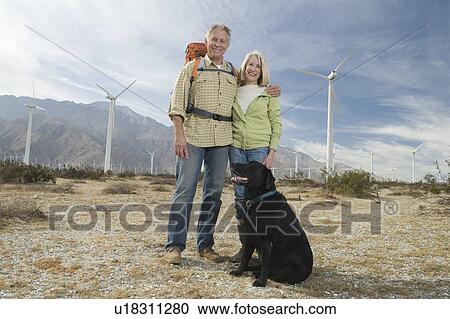 Stock Image - Senior couple with dog near wind farm. Fotosearch