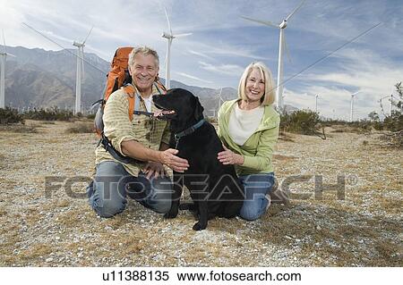 Stock Photography - Senior couple with dog near wind farm. Fotosearch