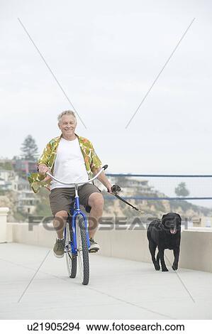Picture - Senior man exercising dog on bicycle. Fotosearch