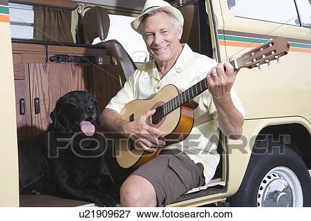 Senior man sits in his campervan with a guitar and his pet dog View Large Photo Image Stock Photo - Senior man sits in his campervan with a guitar and his pet dog. Fotosearch