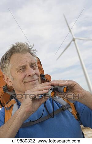 Stock Image - Senior man with backpack near wind farm. Fotosearch