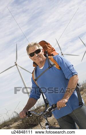 Stock Image - Senior man with bicycle near wind farm. Fotosearch