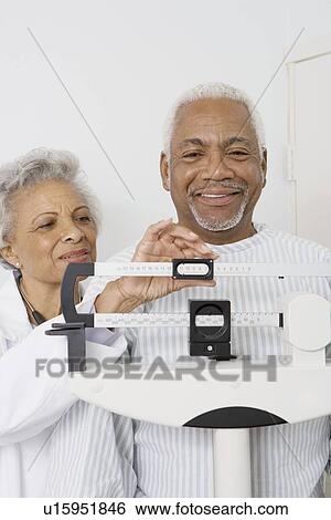 Senior medical practitioner checks weight of patient View Large Photo Image Stock Photograph - Senior medical practitioner checks weight of patient. Fotosearch