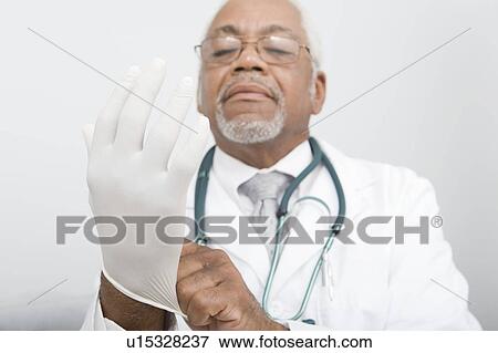 Stock Photo - Senior practitioner pulls on surgical gloves. Fotosearch