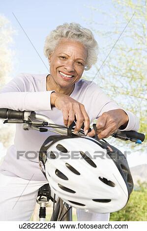 Picture - Senior woman leans on handlebars of mountain bike. Fotosearch
