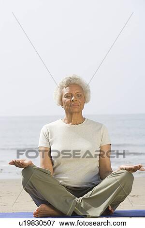 Stock Photo - Senior woman sits with legs crossed in yoga pose. Fotosearch