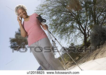 Stock Photography - Senior woman stands on phone with walking poles. Fotosearch