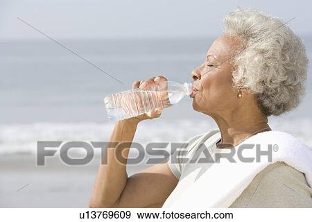 Senior woman stands with drinks water with a towel over her shoulder on beach View Large Photo Image Stock Photo - Senior woman stands with drinks water with a towel over her shoulder on beach. Fotosearch