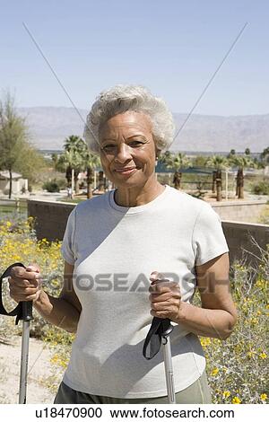 Stock Image - Senior woman stands with walking poles. Fotosearch