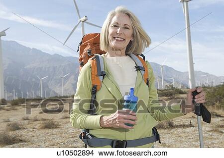 Picture - Senior woman with backpack near wind farm. Fotosearch
